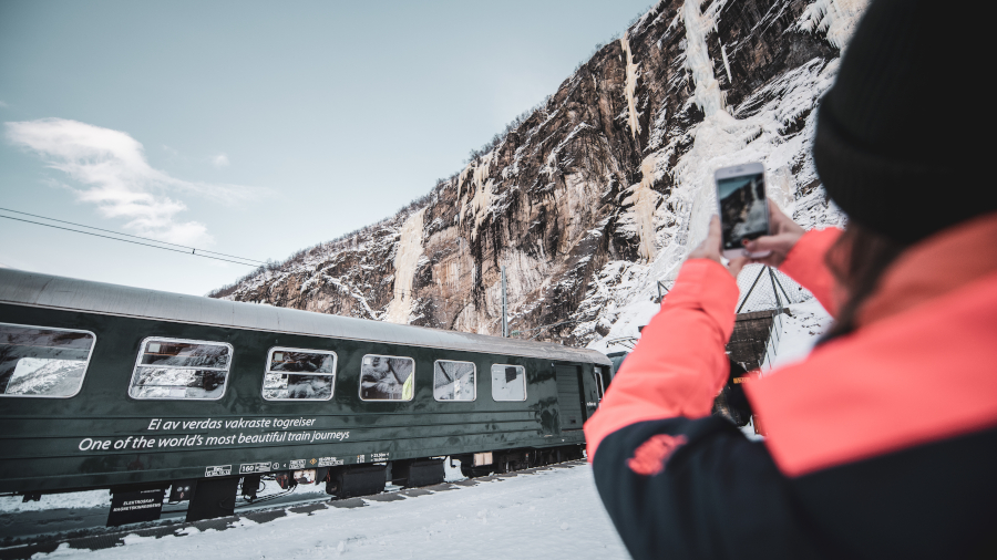 Ei jente tar mobilbilete av Flåmsbana under isdekt fjellside på Kjosfossen